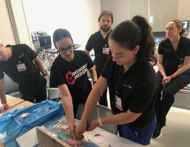 Medical residents in a simulation lab practicing a hands-on procedure on a training model under faculty supervision.