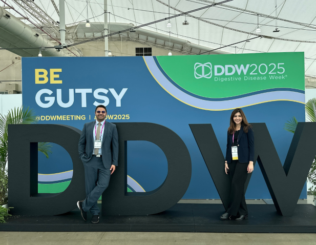 Male and female internal medicine residents in front of DDW2025 signage for Digestive Disease Week conference..